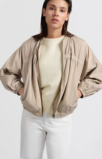 A women's lightweight bomber jacket in a soft beige color with a relaxed, slightly oversized fit. It features a round neckline, a full-length front zipper, and gathered detailing along the chest for a subtle textured effect. The long sleeves are voluminous and taper into elasticated cuffs, while the hem also has an elastic finish for a comfortable and slightly cropped silhouette.