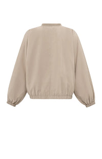 A women's lightweight bomber jacket in a soft beige color with a relaxed, slightly oversized fit. It features a round neckline, a full-length front zipper, and gathered detailing along the chest for a subtle textured effect. The long sleeves are voluminous and taper into elasticated cuffs, while the hem also has an elastic finish for a comfortable and slightly cropped silhouette.