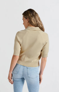 his is a women's short-sleeve zip-up cardigan in a soft, warm beige color. It is made from a finely knitted fabric with a smooth texture and a structured yet comfortable fit. The cardigan features a classic folded collar that sits neatly around the neckline, leading down to a silver-toned full-length zipper at the front, allowing it to be worn open or closed.

The sleeves are elbow-length with a slightly loose fit, finished with ribbed cuffs for a subtle contrast in texture. The hem is also ribbed, giving t
